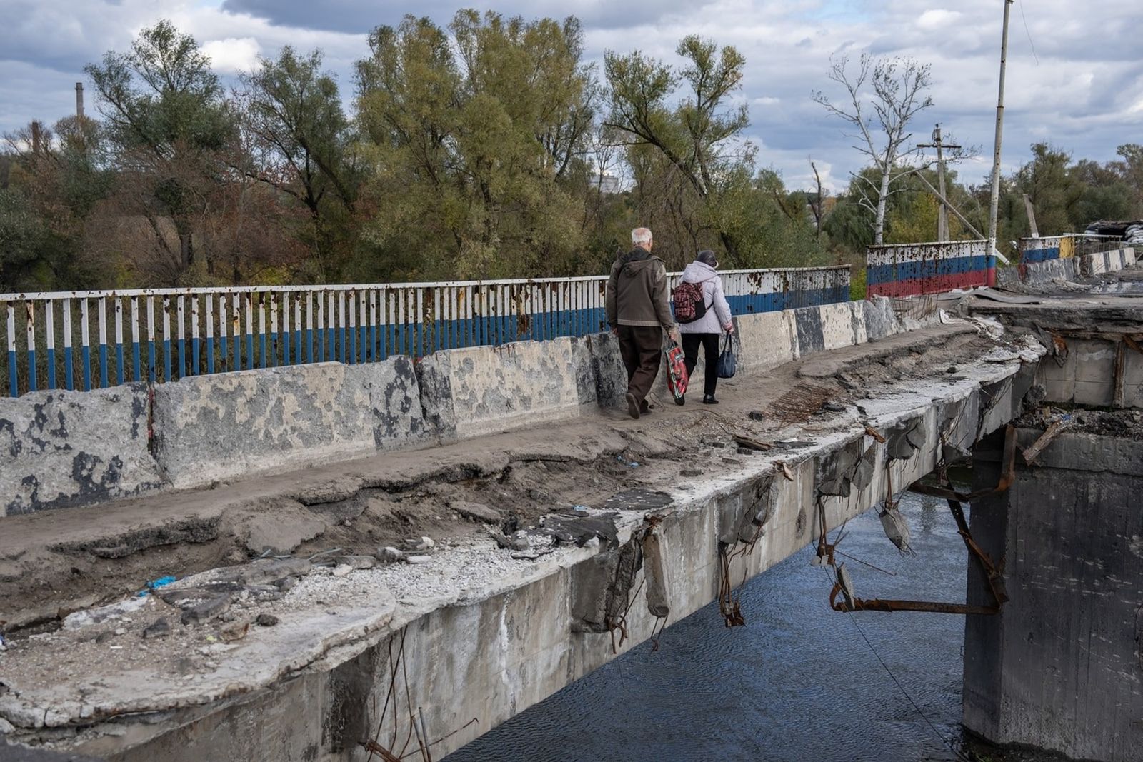 Местные жители переходят реку по остаткам моста, серьезно поврежденного в результате боёв между украинскими и российскими войсками в Харьковской области. 13 октября / Carl Court / Getty Images / Grid