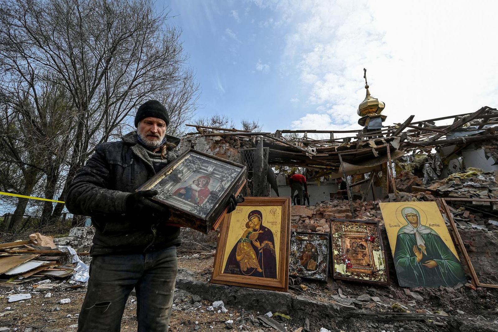 Мужчина на Пасху несет православную икону на фоне разрушенной церкви в селе Камышуваха в Запорожской области. 16 апреля / Reuters