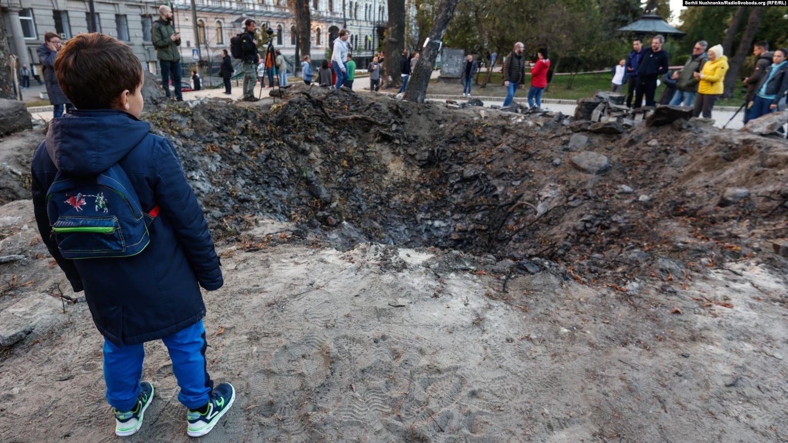 Мальчик осматривает воронку возле детской площадки в парке Тараса Шевченко в Киеве. Позже люди оставили здесь цветы - в память о погибших во время нападения. Снаряды российских ракет попадали не только по объектам энергетической инфраструктуры, но и 