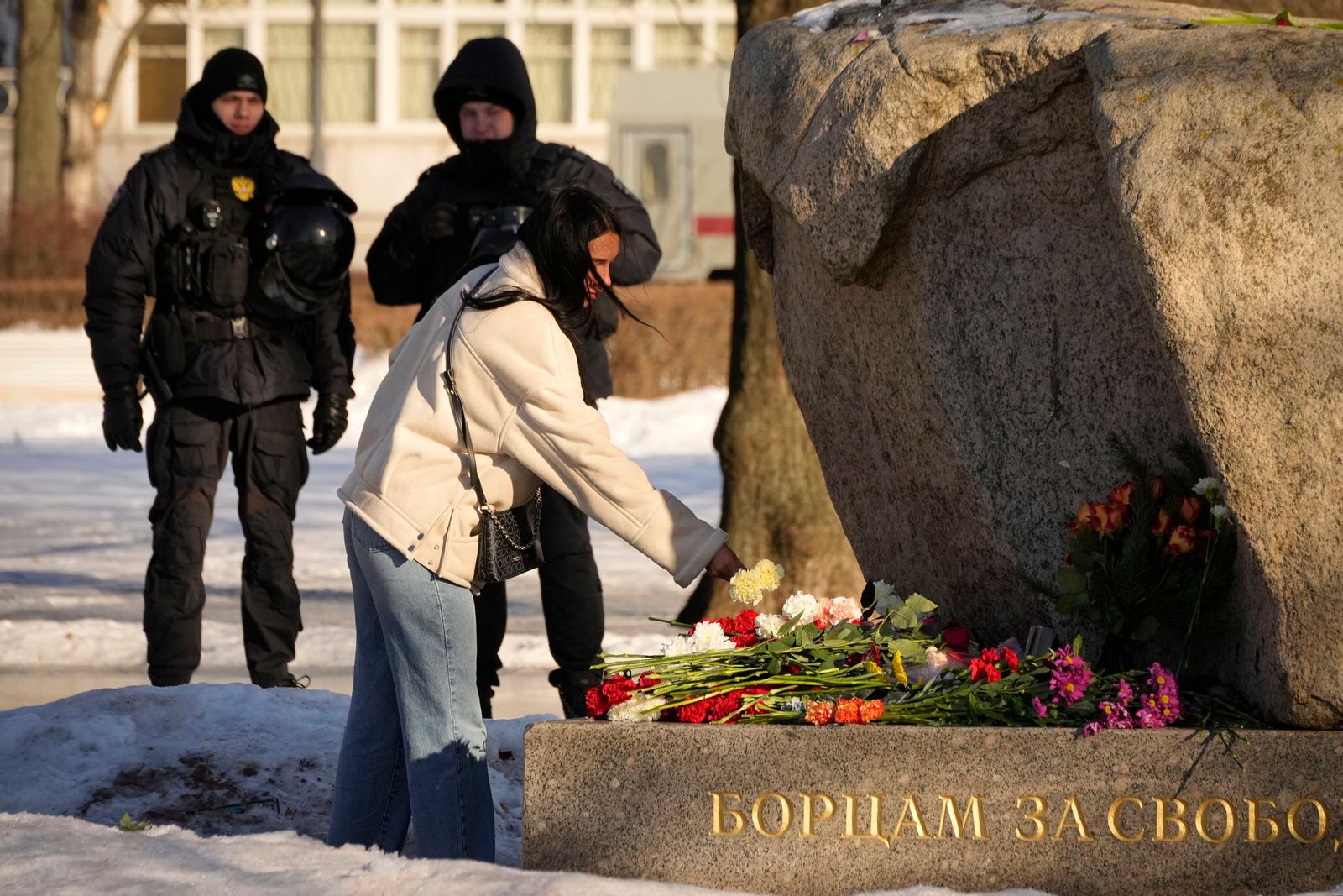 Сотрудники полиции наблюдают за женщиной, возлагающей цветы в знак уважения к погибшему Алексею Навальному у Соловецкого камня в Санкт-Петербурге. 18 февраля / Dmitri Lovetsky / AP Photo