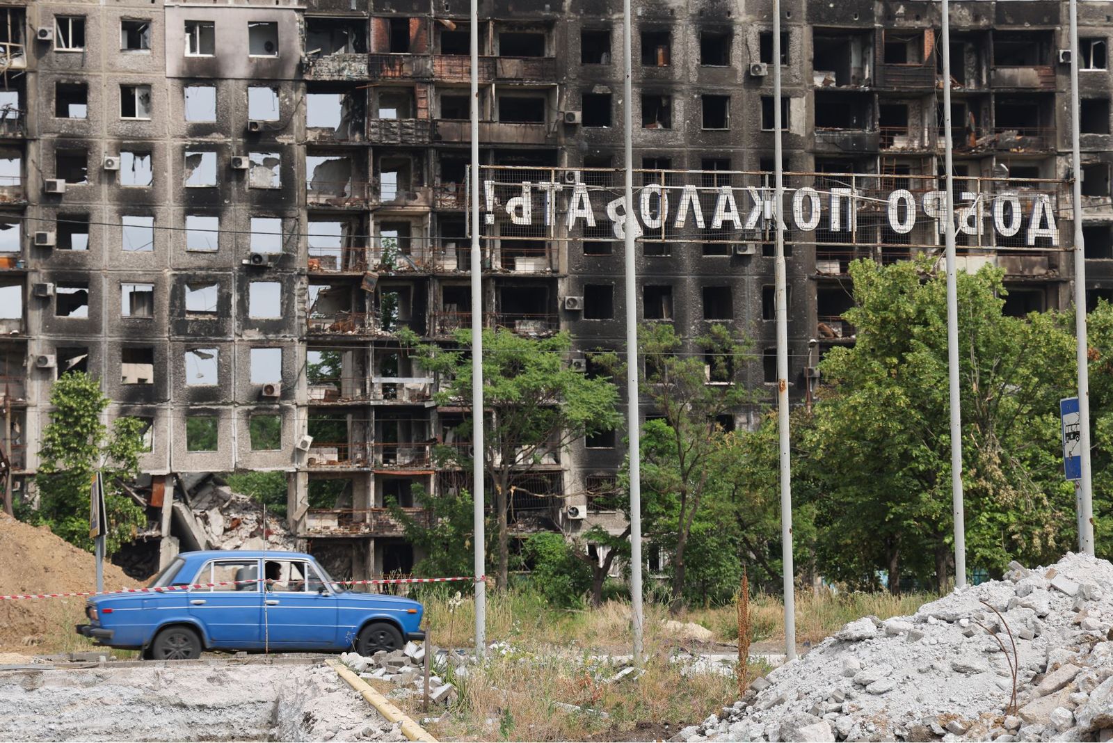 Надпись «Добро пожаловать!» на фоне жилого дома, разрушенного в результате обстрела Мариуполя. 23 июня / Егор Алеев / ТАСС / Meduza