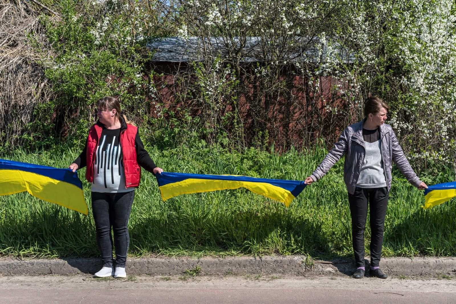 Люди в селе Корнивка стоят вдоль дороги, держа в руках украинские флаги, в ожидании похоронной процессии погибшего Егора Бартоша. 25 апреля / The New York Times