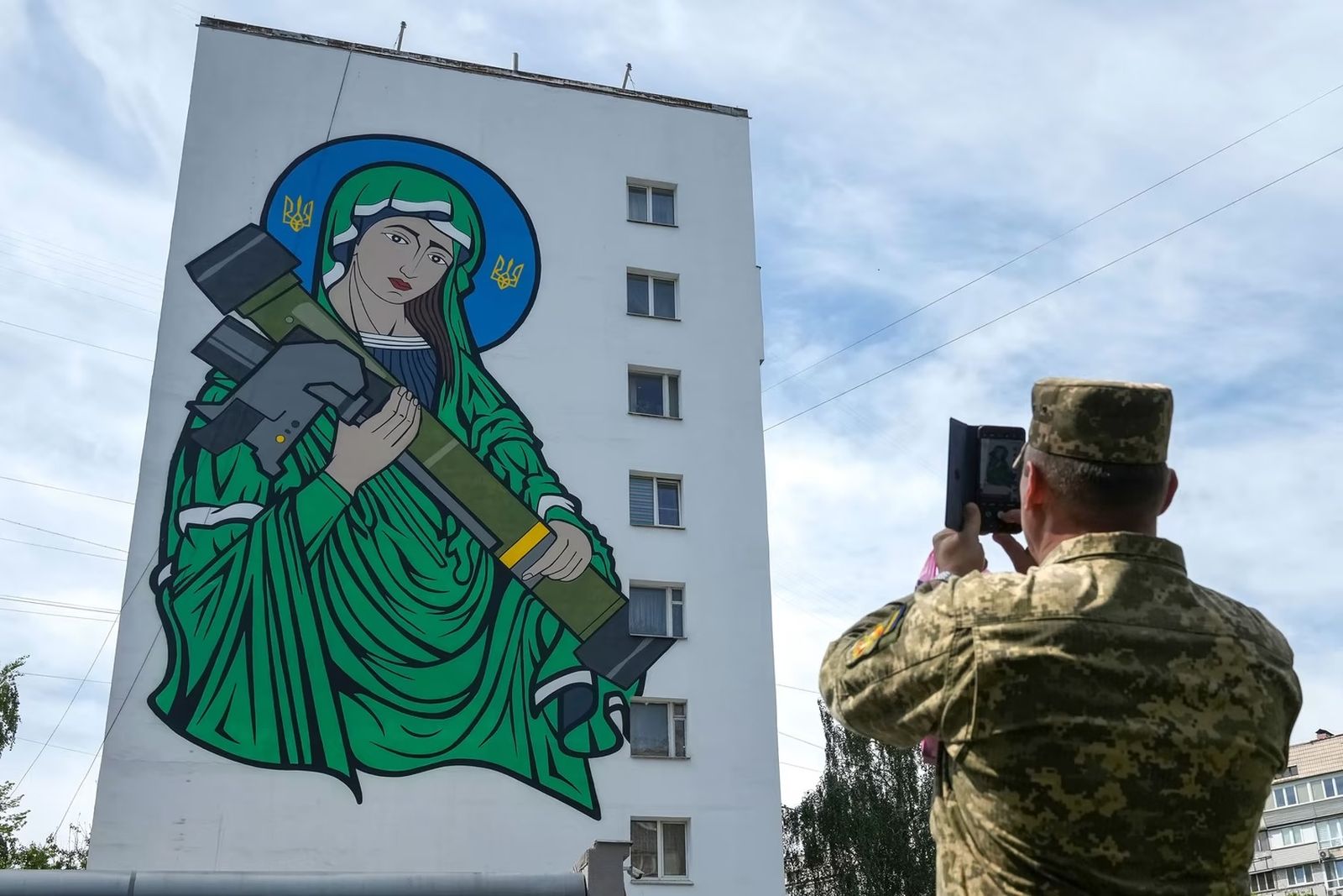 Украинский солдат фотографирует расположенную на стене жилого дома фреску под названием «Святая Джавелина», которая посвящена американской переносной ракете класса «земля-воздух». Работа иллюстратора и художника Криса Шоу отсылает к ракете Javelin, п