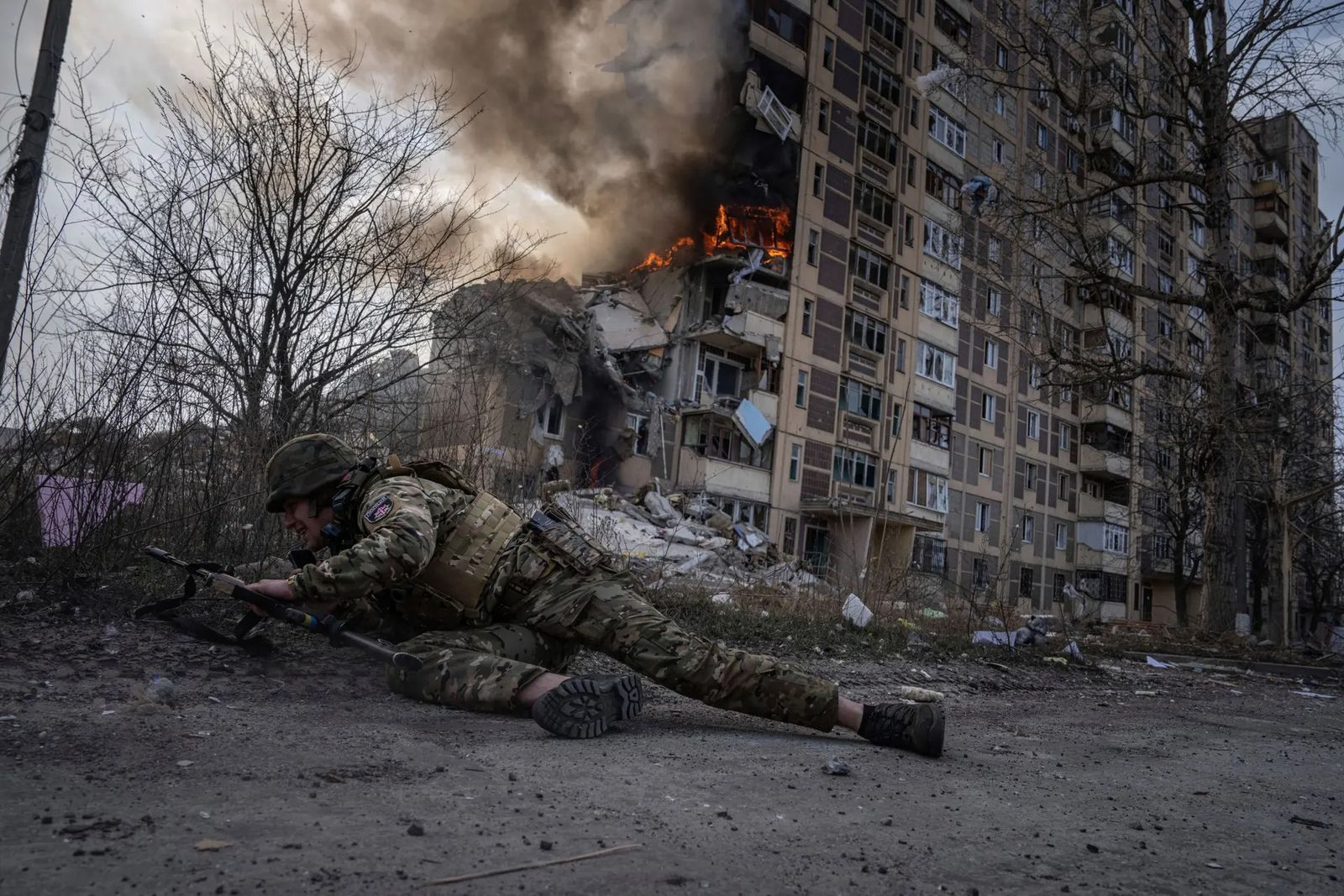 Военный укрывается перед горящим зданием, пострадавшим от авиаудара в Авдеевке. 24 марта / Evgeniy Maloletka / AP Photo / The Guardian